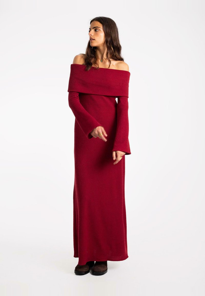 Robe longue rouge décolletée, confectionnée dans un tissu doux, avec de longues manches à poignets évasés et une silhouette ajustée.