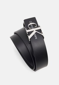 Cintura in pelle nera con una fibbia e dettagli del logo "CK" in tonalità argento. Texture liscia con lunghezza regolabile.