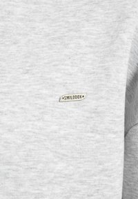 Tessuto di felpa grigio con una morbida texture. Presenta una piccola etichetta ricamata "SMILODOX" sul fronte. Design semplice e privo di decorazioni.