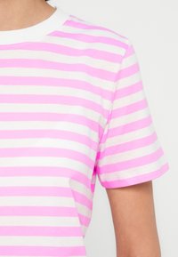 Kortermet T-skjorte med rosa og hvite horisontale striper. Stoffet er myk bomull med en klassisk rund hals.