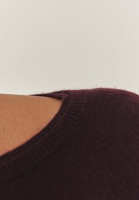 Burgundijas adīts krekls ar noapaļotu apkakli un redzamu dūriņu rakstu. Satur nelielu izgriezumu uz pleca.