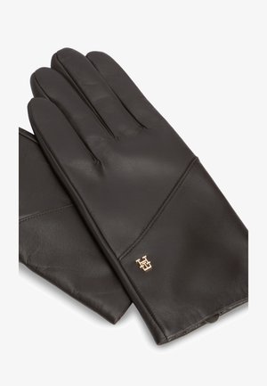 Een paar zwarte leren handschoenen met een klein goudkleurig decoratief embleem op het polsgebied, afgebeeld op een witte achtergrond.
