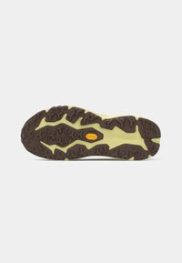 Sola de um sapato de trail running em castanho e amarelo claro, apresentando padrões de aderência texturizados e um logótipo proeminente, projetado para tração e estabilidade.