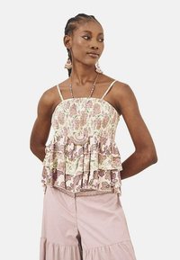 Top de tirantes con estampado floral y volantes en colores pastel. Tirantes transparentes y cuerpo fruncido. La modelo lleva pendientes a juego y cuentas en capas.