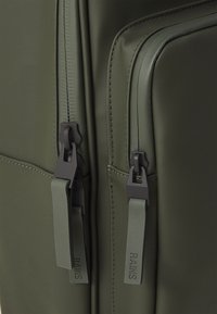 Sac de voyage vert olive en matériau synthétique lisse, avec des fermetures éclair sombres contrastantes et des tirettes de fermeture éclair de marque portant le texte "RAINS."