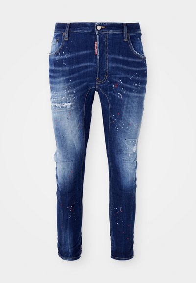 Dark blue slim-fit jeans with faded areas, paint splatters in white, red, and black, and a distressed patch on the left thigh.