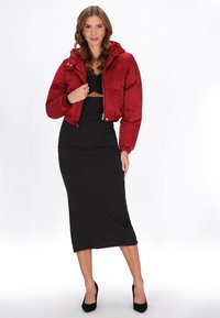 Rød puffjakke med hætte, cropped design og elastiske manchetter, parret med en sort tætsiddende kjole og sorte højhælede sko.