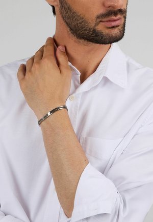 Bracciale in tono argento dal design elegante, con maglie alternate lucide e texture, indossato su un braccio di pelle chiara.