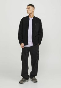 Black zip-up jacket with a pocket, light purple t-shirt underneath, baggy black cargo pants with side pockets, and gray sneakers.