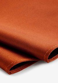 Tekstilstof i varm terracotta, med en glat, struktureret vævning og synlige sømme langs de krøllede kanter.
