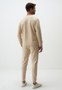 Felpa sportiva beige e pantaloni coordinati in morbido tessuto, con colletto a girocollo e polsini aderenti, abbinati a sneaker bianche.