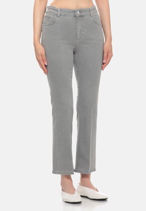 Donna con jeans grigi a gamba dritta e scarpe bianche con tacco basso, in piedi con le mani rilassate lungo i fianchi.