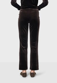 Čierne zamatové rozšírené nohavice s hladkým povrchom a elastickým pásom. Nosené s hnedými mokasínami s nitmi na zadnej strane.