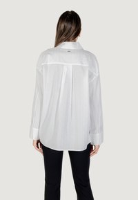Camicia bianca a maniche lunghe con motivo testurizzato, polsini con bottoni, dettaglio sul retro e vestibilità comoda. Abbinata a pantaloni neri.