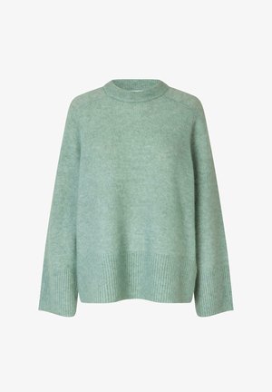 Svetlo zelena pletena jopica s okroglim izrezom. Ima rebraste manšete in spodnji rob, kar zagotavlja teksturno kontrastnost gladkemu telesu.