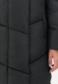 Melna pūkainā jaka ar quilted dizainu, kas izgatavota ar dimanta formas pildījumu un sānu kabatu. Gluda tekstūra un brīva piegriezuma.