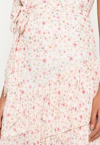 Sukienka w kwiaty z białym tłem i różowymi oraz żółtymi kwiatami, z plisowanym teksturem i wiązaniem w pasie dla regulowanego dopasowania.