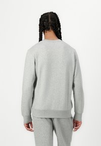 Grå genser i mykt materiale med rund hals, ribbestrikkede mansjetter og nederkant, med en avslappet passform og subtile sømdetaljer.