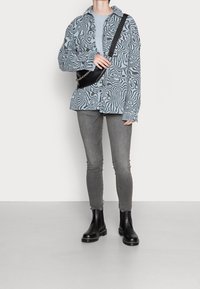 Camisa con patrón de olas en azul y negro, combinada con jeans skinny grises y botas de tobillo negras. El accesorio es un pequeño bolso cruzado negro.
