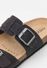 Sandal in suede nero con due cinturini regolabili, fibbie in metallo silver, sole in sughero e suola in gomma nera. Design testurizzato e flat.