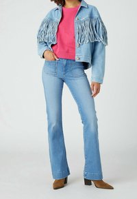 Džínová bunda s třásněmi, světle modrá barva, doplněná růžovou mikinou a rozšířenými světle modrými džíny; hnědé kotníkové boty na vysokém podpatku.