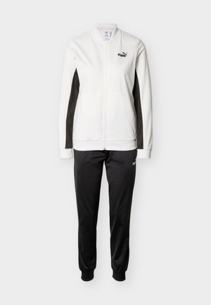 Puma treningsdress i hvitt og svart. Har en jakke med glidelås og svarte sidestykker, samt svarte bukser med elastiske mansjetter. Glatt stofftekstur.