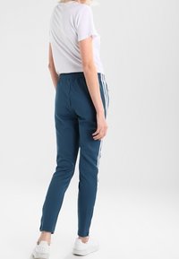 Turkosa träningsbyxor med vita sidostreck, elastisk midja och avsmalnande passform, kombinerade med en enkel vit t-shirt och vita sneakers.