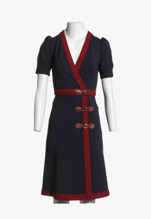 Marineblaues Kleid mit kurzen Puffärmeln, tiefem V-Ausschnitt, rotem Besatz, drei roten Schnallenverschlüssen und rotem Taillenbund auf einer weißen Schaufensterpuppe.