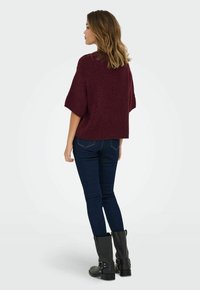 Maglione a maglia bordeaux con una vestibilità comoda, maniche corte e tessuto testurizzato, abbinato a jeans blu scuro e stivali neri al polpaccio.
