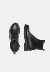 Bottines en cuir noir avec un bout rond, un laçage et une semelle texturée. Fermeture éclair sur le côté et tirant pour faciliter l'enfilage.