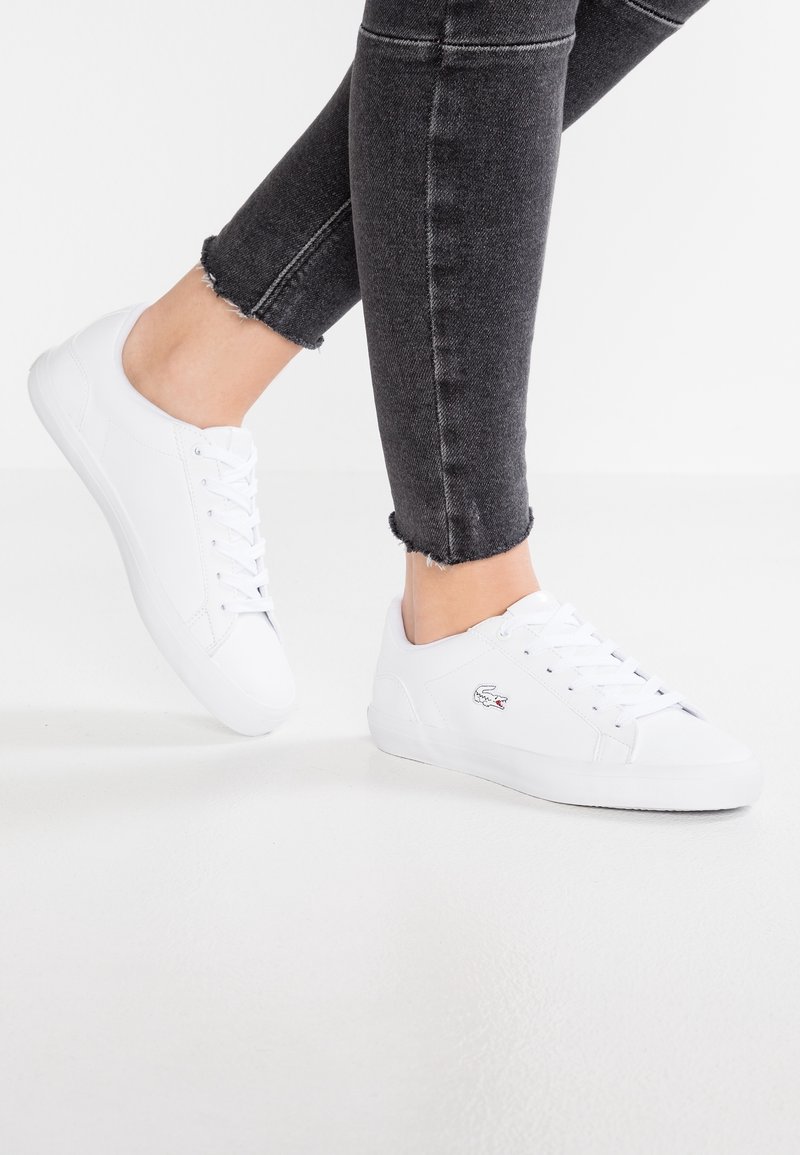 Baskets blanches en cuir lisse, avec un design à lacets, un bout arrondi et un petit logo brodé sur le côté.
