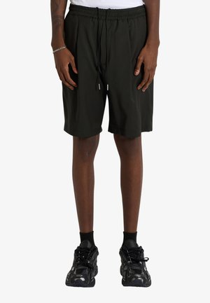 La persona indossa pantaloncini neri con vita elastica e coulisse, scarpe da ginnastica nere, calzini neri e un braccialetto d'argento al polso sinistro.