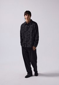 Camicia nera a fantasia con bottoni, dal taglio rilassato, abbinata a pantaloni neri larghi e scarpe slip-on nere. Design semplice e texture liscia.
