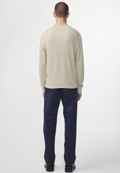 Beiger Strickpullover mit strukturierter Oberfläche, lockerer Passform und geripptem Kragen, kombiniert mit dunkelblauen, weit geschnittenen Hosen.