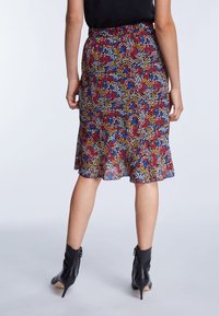 Jupe midi florale avec un imprimé multicolore de feuilles rouges, bleues et jaunes, fabriquée en tissu léger avec un ourlet évasé. Bottines noires.