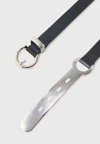 Μαύρη δερμάτινη ζώνη με γυαλιστερή ασημένια πόρπη στη μία άκρη και μακρύ, επίπεδο ασημένιο μεταλλικό άκρο με τρύπες στην άλλη άκρη.