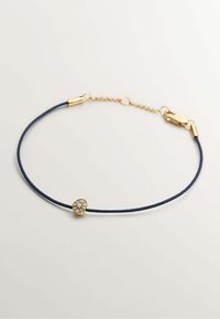 Pulsera de cordón en color navy con un charm dorado que presenta un acento de strass claro en forma circular en un engaste decorativo. Se incluye un cierre de hardware dorado.