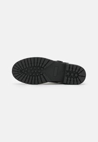 Suela de bota de goma negra con un patrón de relieve texturizado que presenta líneas elevadas y detalles en forma de estrella, diseñada para ofrecer agarre y durabilidad.