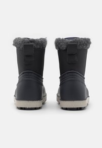 Botas impermeables negras con forro de piel gris y costuras decorativas, vistas desde atrás con una suela texturizada para el agarre.
