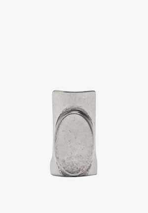 Srebrny metalowy pierścionek o fakturowanej powierzchni, z owalnym wycięciem i zaokrąglonym, krzywym kształtem. Prosta i nowoczesna forma.