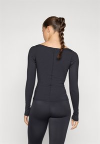 Μαύρη μπλούζα με μακριά μανίκια, ριγωτή υφή, εφαρμοστή σχεδίαση και στρογγυλή λαιμόκοψη. Το πίσω μέρος διαθέτει ραφή και συνδυάζεται με μαύρες κολάν.