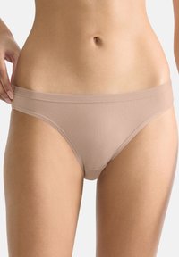 Slip bikini beige senza cuciture con texture liscia, cintura elastica, design a vita bassa e senza dettagli di cuciture visibili.