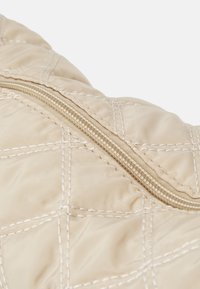 Tessuto trapuntato beige con un motivo di cucitura diagonale e una chiusura con zip lungo il bordo, con una leggera lucentezza e una texture liscia.