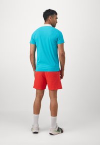 Turquoise polo shirt with a white collar, paired with red shorts. The shirt has short sleeves; the outfit includes white and gray sneakers.