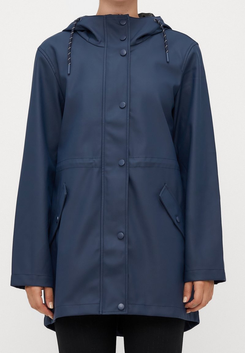 Imperméable bleu marine à capuche, avec fermeture à boutons-pression sur le devant et poches à rabat, porté par une personne des épaules jusqu'au milieu des cuisses.