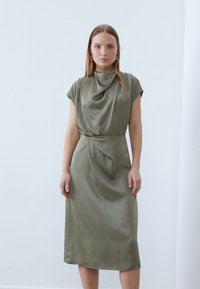 Olive green midi dress in smooth satin with a cowl neckline, cap sleeves, and a gathered waist, featuring subtle draping and a tapered hem.