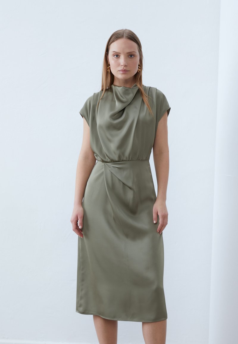 Olive green midi dress in smooth satin with a cowl neckline, cap sleeves, and a gathered waist, featuring subtle draping and a tapered hem.
