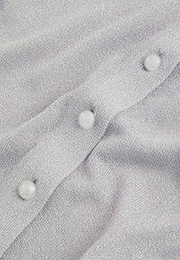 Lys grå strikket stof med en glitrende tekstur, prydet med tre hvide knapper langs en stolpe. Blød og glat udseende.