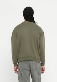 Felpa verde oliva realizzata in tessuto morbido, caratterizzata da una vestibilità ampia, spalle ribassate e polsini a costine all'orlo e alle maniche.