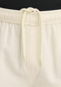 Pantalone kremaste boje s teksturom i strukom na uzicu. Tkanina ima suptilne horizontalne pruge i glatke krajeve na uzici.